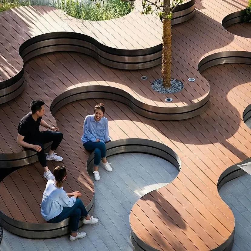 Three people sitting and talking on curved timber benches on a decked roof terrace, seen from above, with a palm tree growing up through the deck.
