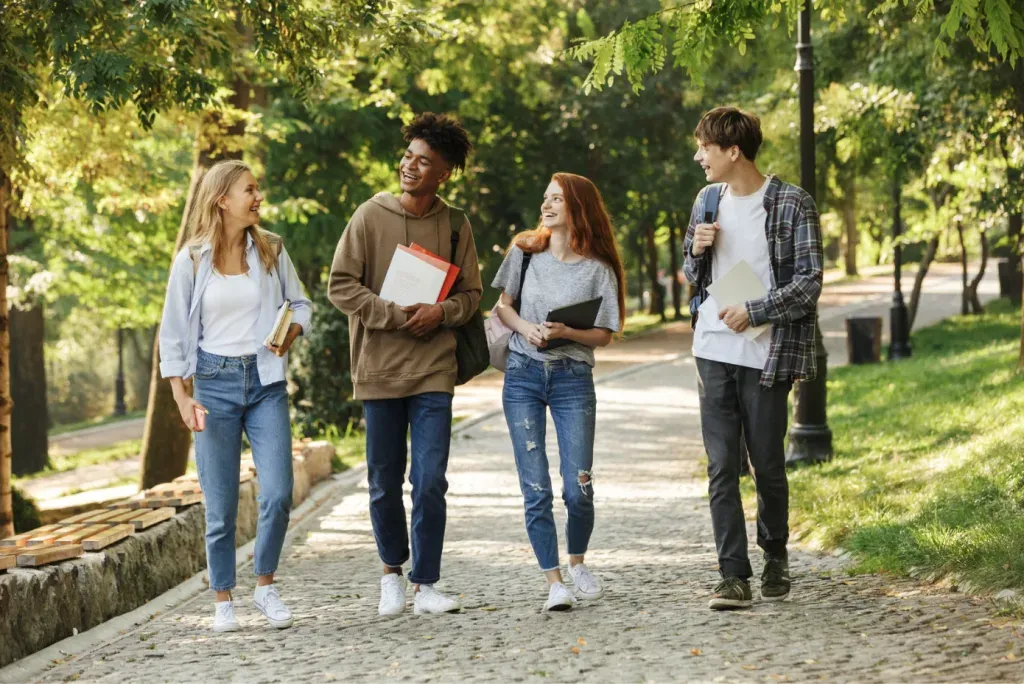 Four students walking a sunlit cobbled path through a park, talking as they go.