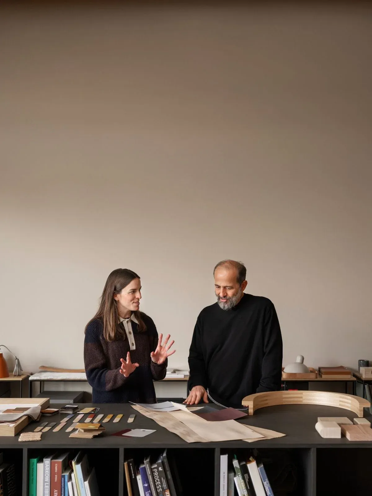 Two colleagues discussing material samples laid out across a large studio table.