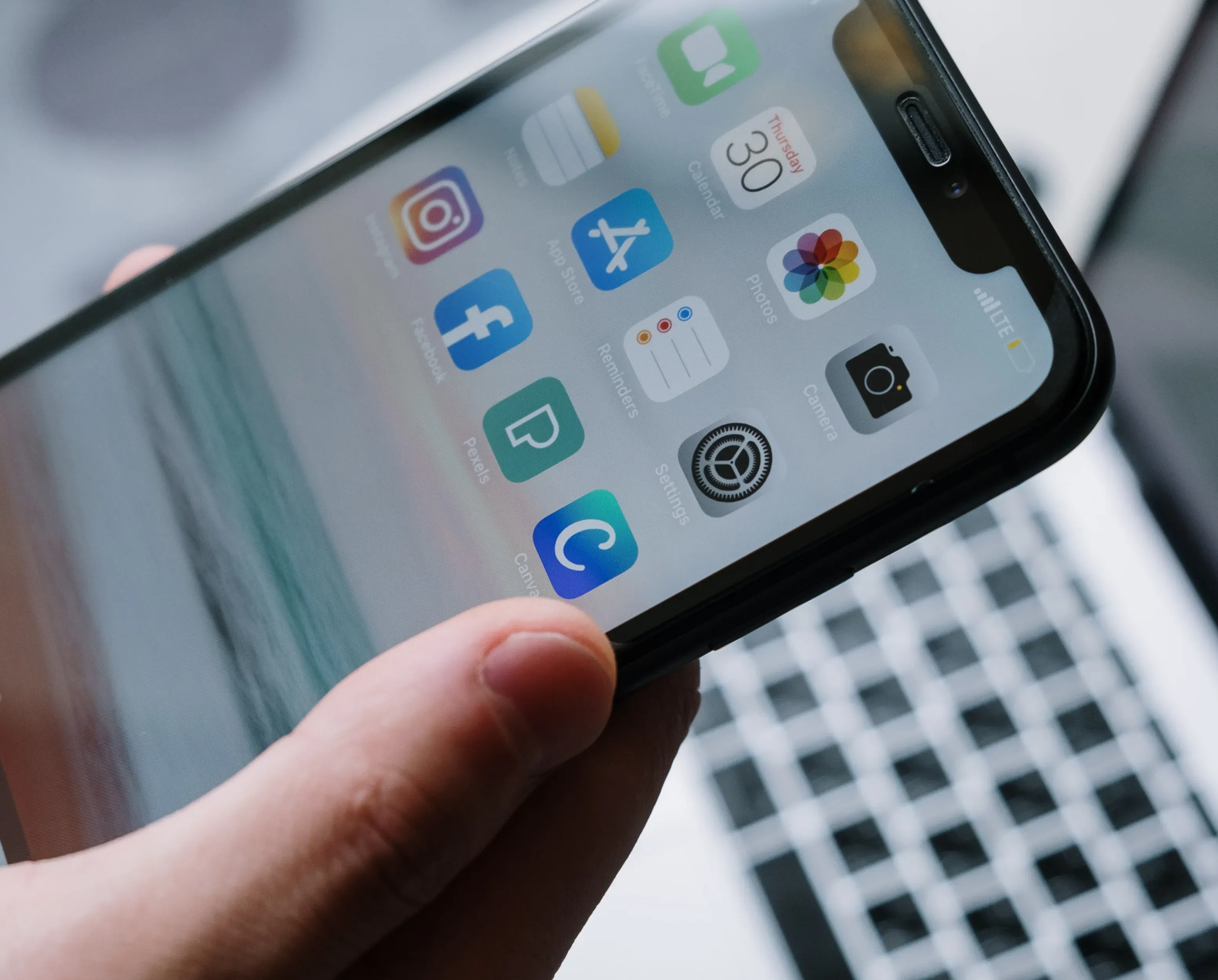 A hand holding a phone, close in on a home screen of app icons.
